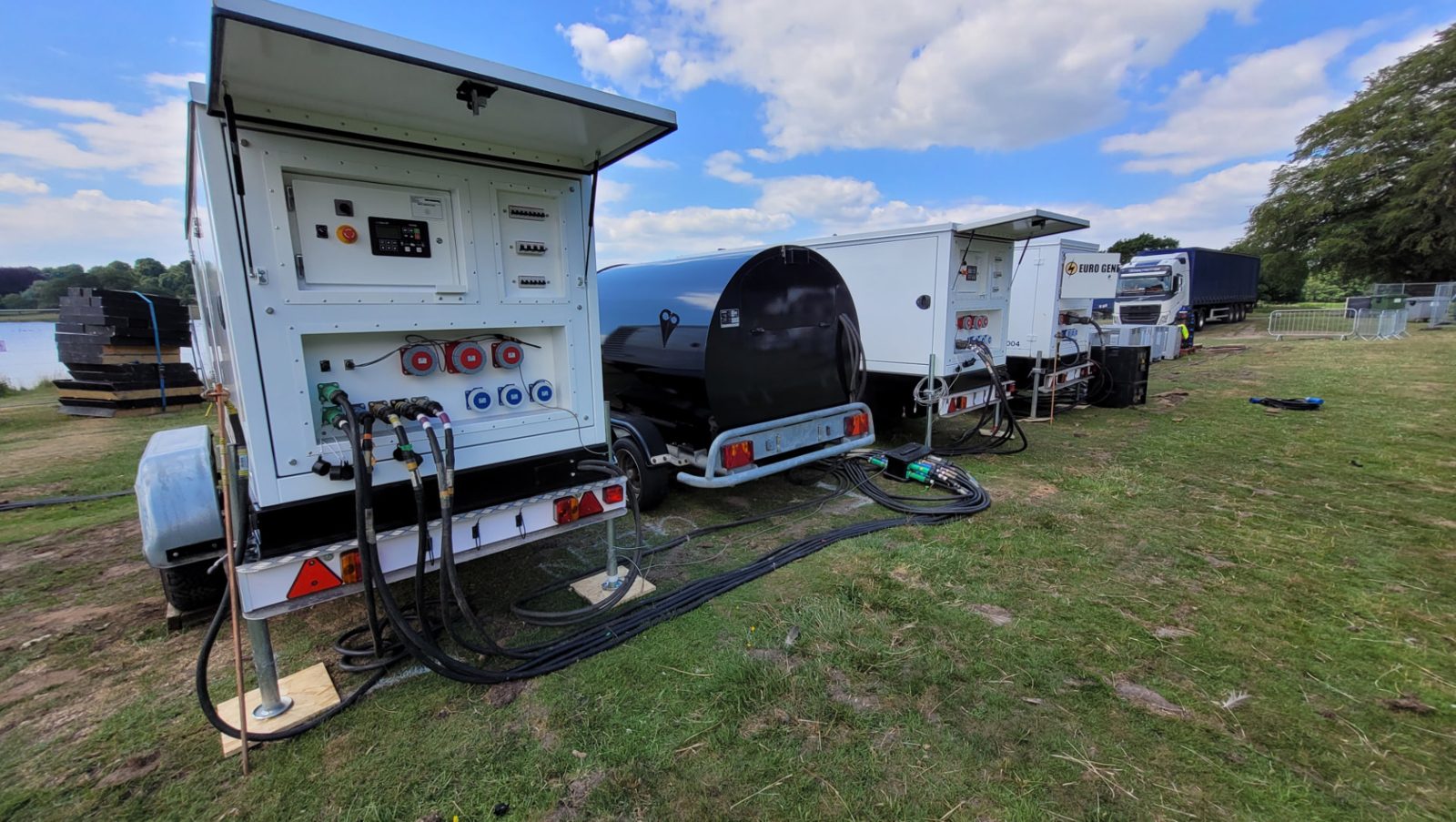Trailer sets and fuel bowser lined up at a lakeside event